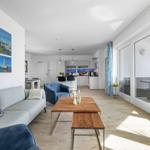Wohnbereich mit Sofa, Couchtisch und Küchenbereich. Große Fenster mit Meerblick.