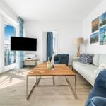 Wohnzimmer mit Sofa, Couchtisch und Fernseher. Große Fenster mit Meerblick.