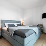 Schlafzimmer mit Bett, Nachttisch und Fernseher an der Wand.