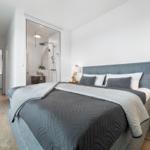 Schlafzimmer mit Doppelbett, Nachttisch und Blick in Bad und Küche.