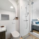 Badezimmer mit Dusche, Waschbecken und Toilette. Spiegel und moderne Einrichtung.