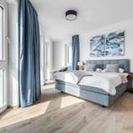 Schlafzimmer mit Blick aufs Meer, blauer Bettwäsche und Wandbild mit Fischen.