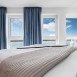 Schlafzimmer mit Blick aufs Meer durch drei Fenster. Bett mit gestreifter Bettdecke.