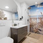 Badezimmer mit Dusche, Waschbecken und Spiegel. Wandbild zeigt Strand.