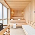 Sauna mit Holzbanken, Fenster und Heizung. Handtücher und Eimer sind vorhanden.