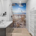 Badezimmer mit Dusche und Seeblicktapete. Waschbecken, Spiegel und Heizkörper sichtbar.