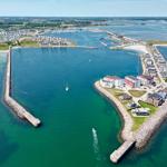 Aerial view of a harbor with boats, waterfront buildings, and surrounding green areas.