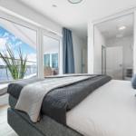 Schlafzimmer mit Blick auf Wasser, großes Bett und angrenzende Dusche.