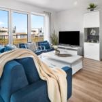 Wohnzimmer mit blauem Sofa, TV und Blick auf Balkon und Meer.