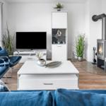 Wohnzimmer mit Sofa, Fernseher, Kamin und großen Fenstern.