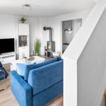 Wohnzimmer mit blauem Sofa, Fernseher und Kaminofen. Holztreppe führt nach oben.