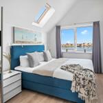 Schlafzimmer mit Dachfenster, Bett und Fenster mit Blick auf Wasser.