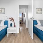 Zwei Schlafzimmer mit blauen Betten und Holzboden. Durchgang zu weiterem Raum.