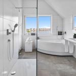 Badezimmer mit Dusche, Badewanne und Fensterblick auf Wasser.