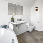 Bad mit Badewanne, Waschbecken und Sauna. Holztür und weiße Fliesen.