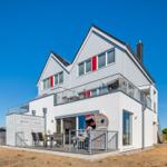 Modernes Haus mit Balkon und Terrasse unter blauem Himmel.