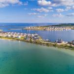 Aerial view of waterfront houses and calm waters under a partly cloudy sky.