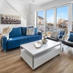 Ein Wohnzimmer mit blauem Sofa, schwarzen Sesseln und großen Fenstern zur Terrasse.