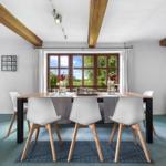 Esszimmer mit Holzdeckenbalken, Tisch mit Stühlen und Blick auf grüne Landschaft.