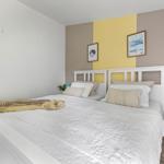 Schlafzimmer mit weißem Bett, gelb-brauner Wand und Nachttisch mit Lampe.