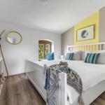 Schlafzimmer mit weißem Bett, Holzboden und gelbem Wandabschnitt.