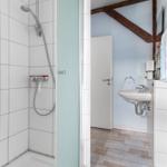 Bad mit Dusche, Waschbecken und Holzbalken an der Wand