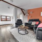 Wohnzimmer mit schwarzen Ledermöbeln, orangefarbener Wand und Holzboden.
