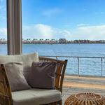 Rattan-Sofa mit Kissen auf Terrasse mit Blick auf Wasser und gegenüberliegende Gebäude.