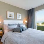 Schlafzimmer mit Bett, Nachttisch und Blick auf den Strand.