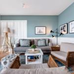 Wohnzimmer mit Sofa, Sessel und Couchtisch. Wandfarbe blau, Holzfußboden und Fenster mit Jalousien.