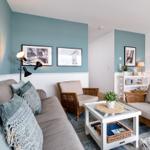 Wohnzimmer mit Sofa, Sessel und Couchtisch. Wandfarbe blau-weiß. Bilder an der Wand.