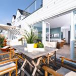 Terrasse mit Tisch, Stühlen und Sonnenschirm. Durchgang in Wohnbereich mit Sofa und Wandbildern.
