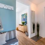 Eingangsbereich mit Sitzbank, Garderobe und Spiegel. Holzfußboden und weiße Wände.