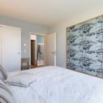 Schlafzimmer mit Bett, Kleiderschrank und Wandbild mit Schiffen.
