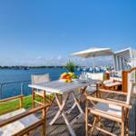 Terrasse mit Tisch, Stühlen und Sonnenschirm am Wasser