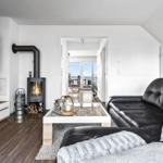Wohnzimmer mit schwarzer Ledercouch, Holzboden und Kaminofen. Durchgang zum Balkon mit Blick.