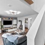 Wohnzimmer mit Sofa, Fernseher und Kamin. Holztreppe führt zur oberen Etage.