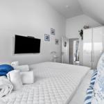 Schlafzimmer mit Bett, TV und Kleiderschrank. Handtuchrollen und maritimes Kissen.