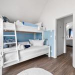 Zimmer mit Doppelstockbett, blauer Wand und Holzboden. Tür führt in ein weiteres Zimmer.