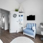 Kinderzimmer mit blau-weißem Sofa, TV und Schreibtisch. An Decke hängt ein Segelbootmodell.