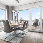 Essbereich mit Tisch und Stühlen, große Fenster zur Terrasse und Blick auf Wasser.