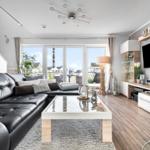 Wohnzimmer mit schwarzer Ledercouch, Glas-Tisch und Fernseher an der Wand.