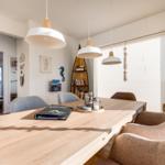 Essbereich mit Holztisch, Stühlen und hängenden Lampen. Fenster mit Jalousien und Seerosen-Dekoration.