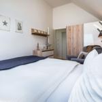 Schlafzimmer mit Bett, Wandbildern und Schrank. Holzregal und Beleuchtung sichtbar.