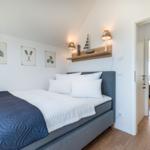 Schlafzimmer mit Bett, Wandbildern und Nachttischen. Durchgang in einen weiteren Raum.