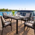 Terrasse mit Tisch und Stühlen, Blick auf Wasser und Ufer.