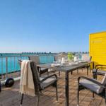 Terrasse mit Tisch, Stühlen und Meerblick. Gelber Schuppen und Sonnenschutz.