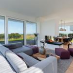 Wohnbereich mit Sofa, Kamin und Blick auf den Strand.