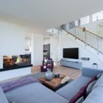 Wohnzimmer mit Kamin, Sofa und Treppenhaus. Wandkarte und Fernseher sichtbar.