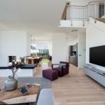 Wohnbereich mit Kamin, TV und Balkonzugang. Holzboden und moderne Einrichtung.